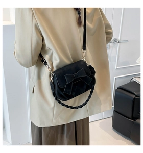 Detail of a black matte crossbody bag featuring a large bow and woven top handle