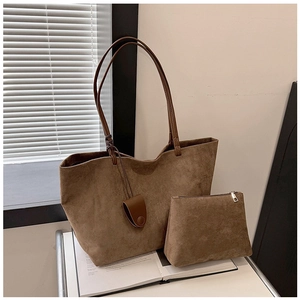 Detailed view of brown suede tote bag and matching pouch set on stacked books