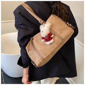 Detail of a brown suede tote bag with a cute white bunny charm worn by a model