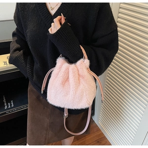 Pink plush drawstring bucket bag with leather handles shown in a cozy indoor setting