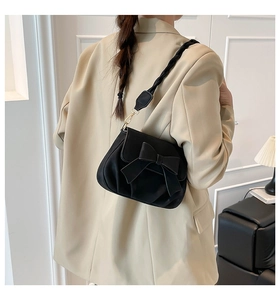 Detail of a black saddle bag with bow and woven strap on a beige blazer background
