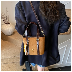 Dettaglio di una borsa a secchiello in camoscio marrone con hardware dorato e perle