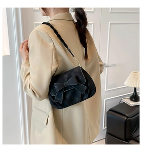 Detail of black bow shoulder bag with woven strap shown on model in beige blazer