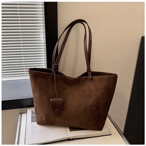 Deep brown suede tote bag with leather straps and decorative tag on white shelf