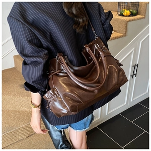 Detail of a large vintage dark brown tote bag with glossy leather texture and drawstring sides