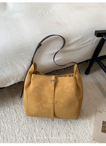 Gros plan d'un sac fourre-tout en daim jaune gingembre avec bandoulière en cuir brun et boucle