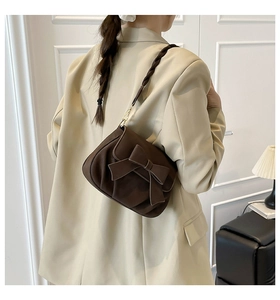 Detail of a dark brown saddle bag featuring a large bow and woven textured strap