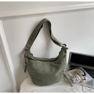 Détail du sac hobo en toile vert foncé avec zip à côté d'un ordinateur et livres