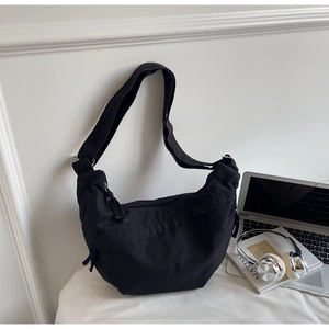 Détail d'un sac bandoulière en toile noire en forme de croissant avec large sangle
