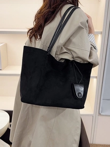 Large black suede tote bag with slim straps and side charms for versatile commuting