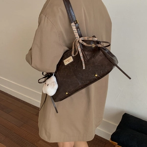 Detail of dark brown embossed shoulder bag with ribbon bow and plush pom-pom charm