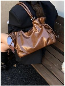 Outdoor shot of a brown glossy leather tote bag with unique drawstring pleats for women