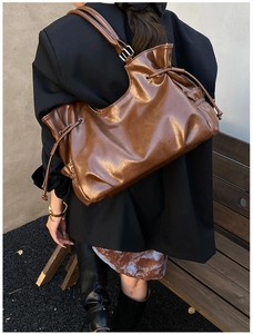 Detail of dark brown tote bag in glossy faux leather on a city street background