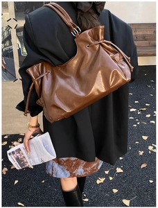 Detail of dark brown tote bag featuring drawstring pleats and metallic eyelet accents