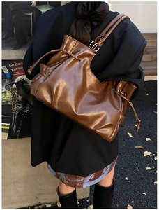 Detail of dark brown glossy bucket bag with drawstring sides and adjustable straps
