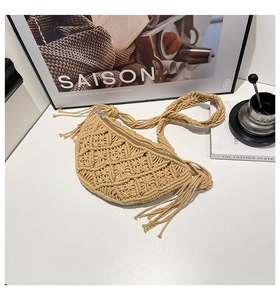 Detail of hand-woven beige straw bag with bohemian tassels on a minimalist white desk