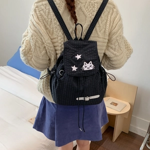 Detail of black plaid drawstring backpack with cartoon cat patch in a cozy home setting
