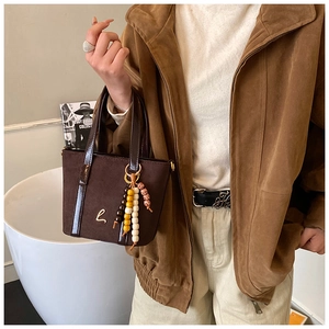 Dettaglio della borsa vintage in pelle scamosciata marrone con logo e nappa di perle
