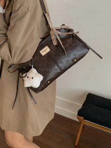 Brown embossed tote bag with cat pattern and plush star charm, worn with khaki coat