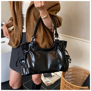 Close-up of black glossy tote bag with decorative side drawstrings and wide handles