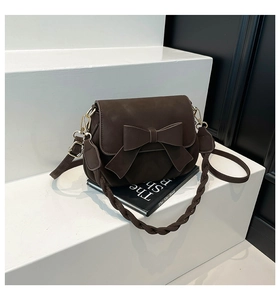 Dettaglio di una borsa a sella marrone scuro opaca con fiocco e manico intrecciato