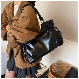 Detail of black glossy drawstring shoulder bag showing its textured pleats and leather finish