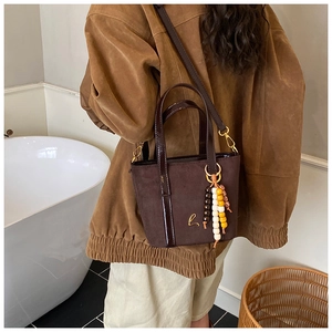 Dettaglio di una borsa tote in pelle scamosciata marrone con materiali misti e ciondolo
