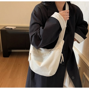 Détail d'un sac bandoulière en toile beige en forme de croissant avec tirette de zip nouée