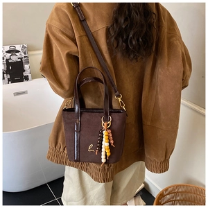 Dettaglio di una borsa tote vintage in pelle scamosciata marrone con ciondolo etnico e logo oro