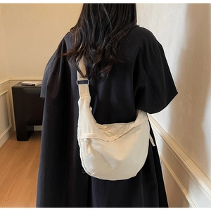 Détail de la bandoulière réglable et forme en croissant du sac à bandoulière en toile blanche