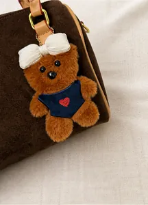 Détail d'un pendentif ours en peluche avec gilet bleu sur un sac à main marron