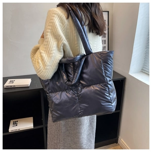 Close-up of quilted puffer tote bag in metallic dark blue shown on model shoulder