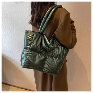 Detail view of large quilted down tote bag in metallic dark green on a shoulder model