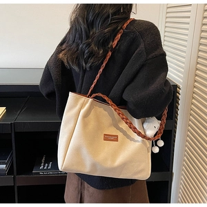 Detail of beige canvas tote bag featuring brown woven strap and cute plush charm pendant