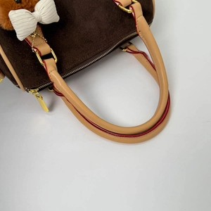 Detailed close-up of brown suede handbag with golden zipper and plush bow accessories
