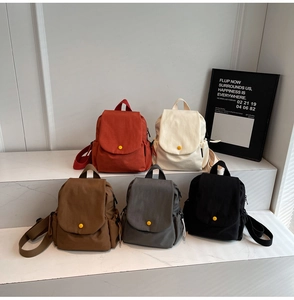 Row of canvas backpacks in five colors displayed on white marble with flap closure