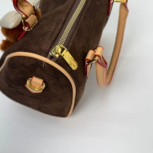 Detail view of brown suede Boston bag with leather trim, gold zipper and plush charm