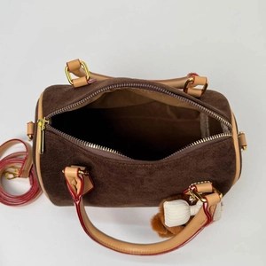 Detail of dark brown suede Boston bag with red trim and golden hardware including long strap
