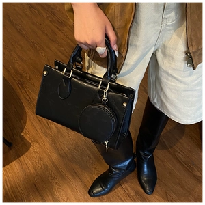 Detail of black leather handbag with gold hardware and detachable mini round pouch charm