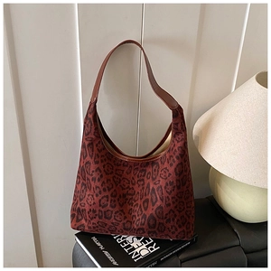 Detail view of large leopard print tote bag with brown leather strap on a decorative book