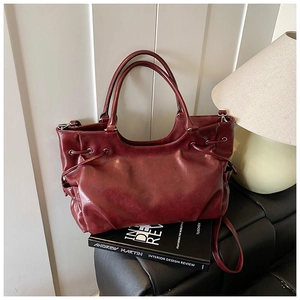 Deep red vintage faux leather tote bag with side drawstring details on a leather bench