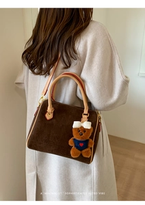 Detail of retro brown suede Boston bag featuring a cute plush bear charm on white coat