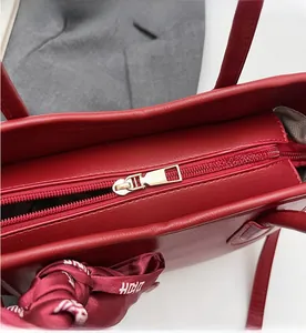 Dettaglio ravvicinato di una borsa in pelle rosso scuro con cerniera dorata e foulard di seta