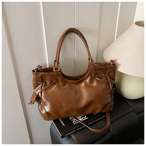 Close-up of caramel brown tote bag with decorative drawstring on a black leather sofa