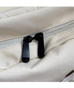 Close-up of smooth dual metal zippers on a cream-colored minimalist canvas backpack