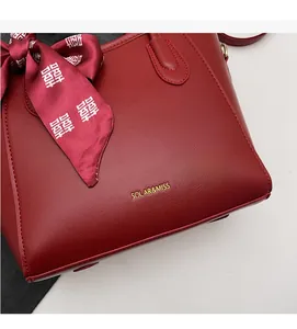 Dettaglio della borsa rossa con trama litchi, logo dorato e nastro decorativo festivo