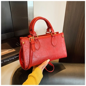 Detail view of red embossed leather handbag with gold studs and adjustable shoulder strap