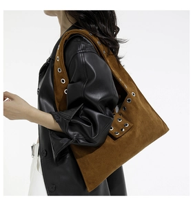 Détail d'un sac d'épaule en daim marron avec œillets argentés porté par un modèle