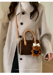 Close-up of brown matte Boston bag featuring a plush bear charm and leather strap