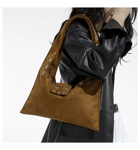 Sac bandoulière en daim marron avec œillets argentés porté par un mannequin chic
